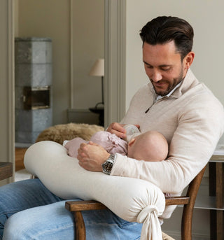 A dad bottle-feeding his baby using a white Nursing Pillow