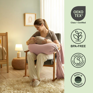 Woman holding a baby with a pink cushion in a room, featuring Oeko-Tex and BPA-Free certification logos bbhugme pregnancy pillow